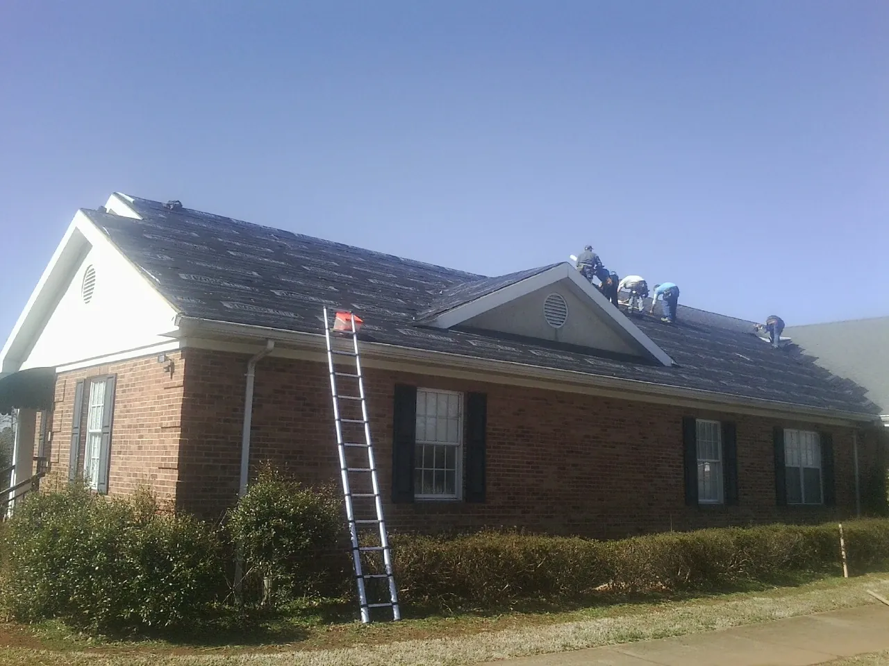 Crew tearing shingles off a brick ranch roof with a ladder set — Metal Roof Repair work by our crew in Plympton