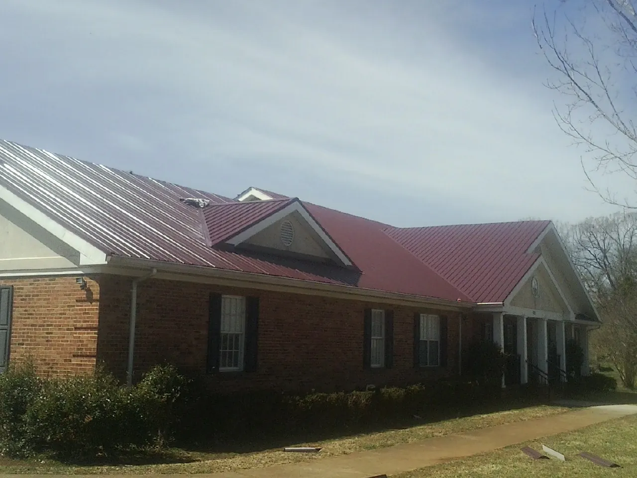 Red metal roof with gabled entries on a long brick building, from a Hail Damage Roof Repair job in Plympton