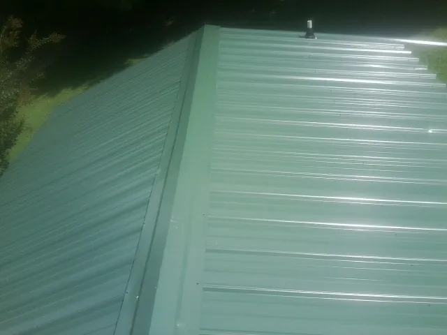 New green metal panels meeting at the ridge of a roof — Flat Roof Repair work by our crew in Plympton