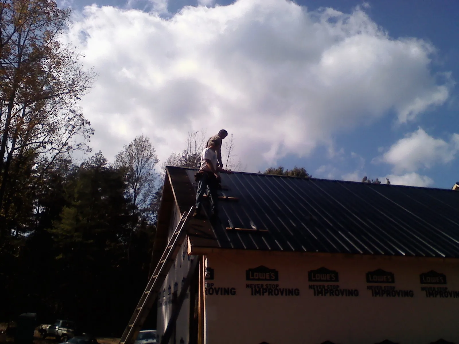 Roofer fastening dark metal panels high against a cloudy sky, from a Roof Inspection job in Plympton
