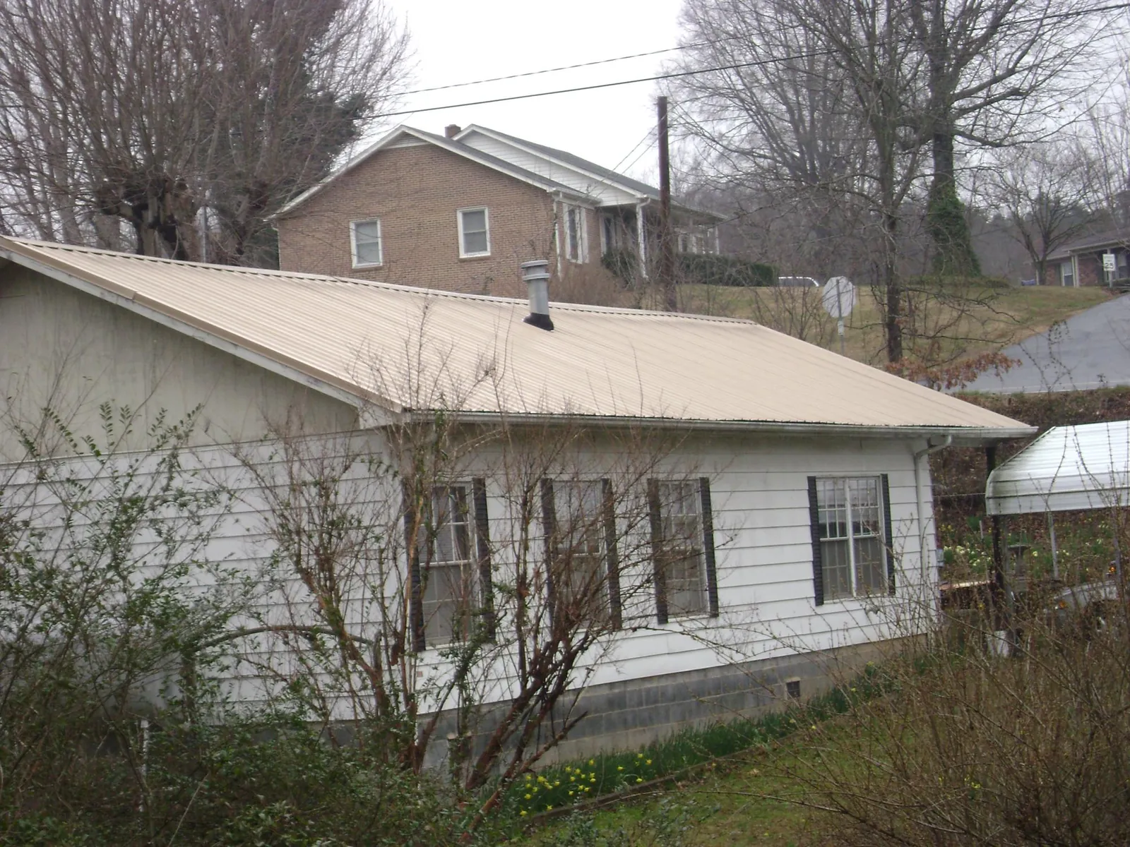Tan metal roof on a white sided house set into a hillside — Commercial Roofing by Roofing Brothers in Plympton